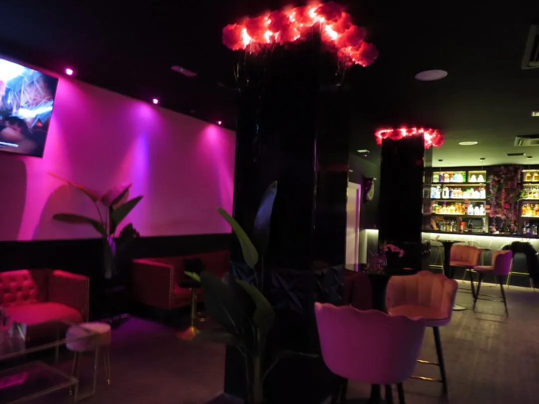 Interior de Capricho con luz rosa, sillones y la barra con botellas al fondo