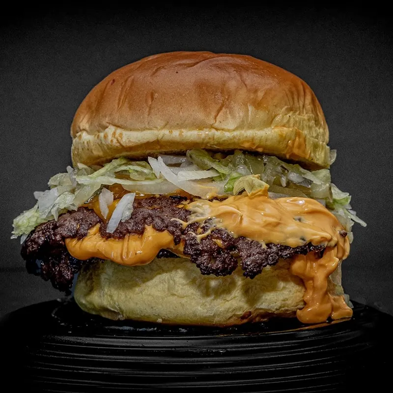 Hamburguesa Big Grotta con lechuga, cebolla y salsa de queso cheddar cayendo por el pan
