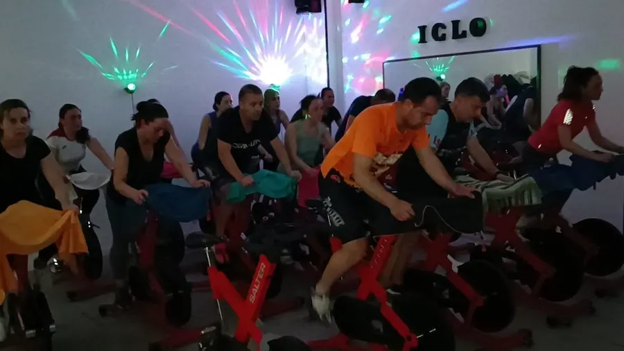 Clase de spinning en Loles Jiménez GYM & PILATES: un grupo de socias y socios pedaleando en bicicletas rojas con luces de colores en la pared