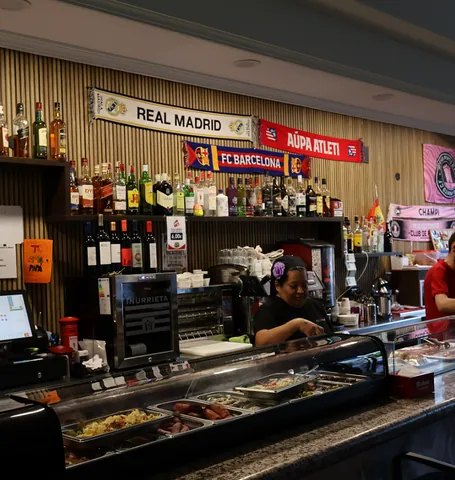Barra del bar con botellas, bufandas de equipos de fútbol y una vitrina de tapas