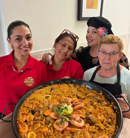 Cuatro trabajadoras del bar sonriendo con una paella con gambas