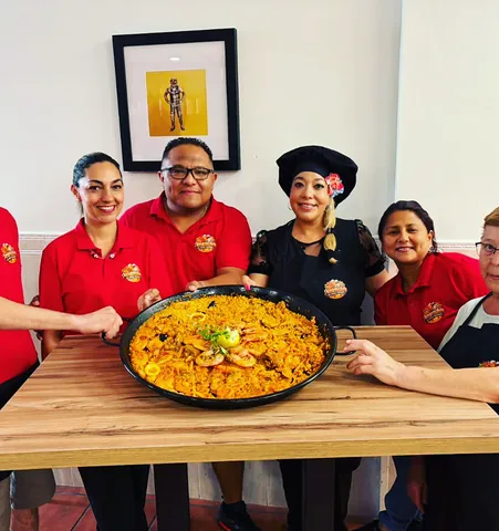 El equipo del bar, con polos rojos, junto a una paella grande sobre la mesa