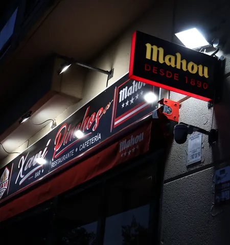 Fachada del bar de noche, con el rótulo de Xavi Pinchos y el cartel de Mahou