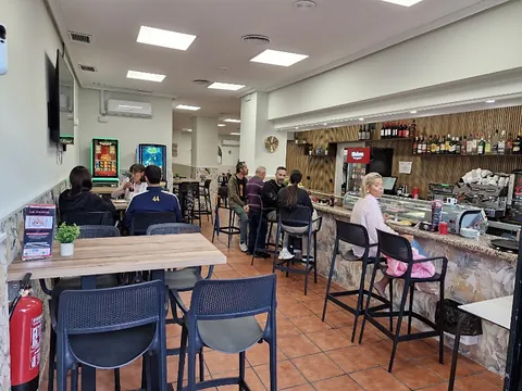 Interior del bar con mesas altas, taburetes y la barra al fondo