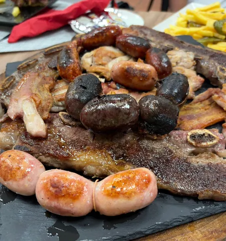Fuente de parrillada con chuletón, chorizos, morcillas y patatas fritas sobre una pizarra