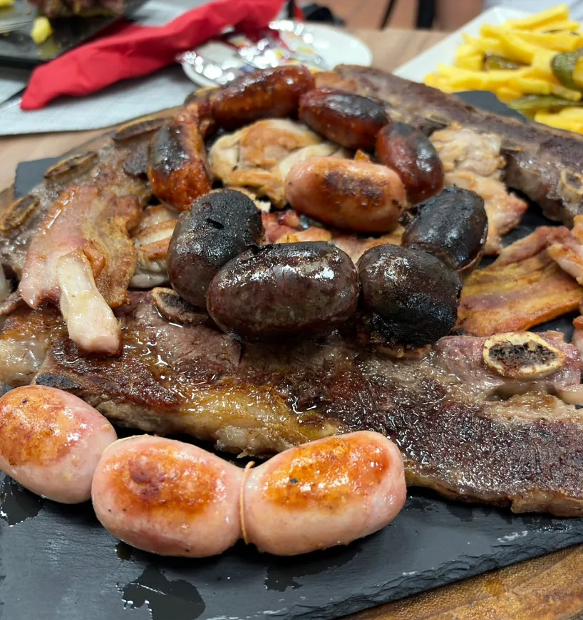 Fuente de parrillada con chuletón, chorizos, morcillas y patatas fritas sobre una pizarra